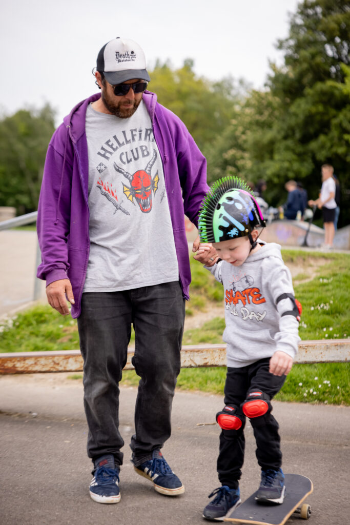 Skateboard coach Rick assisting a young child with their first skateboard pushes during a lesson.
