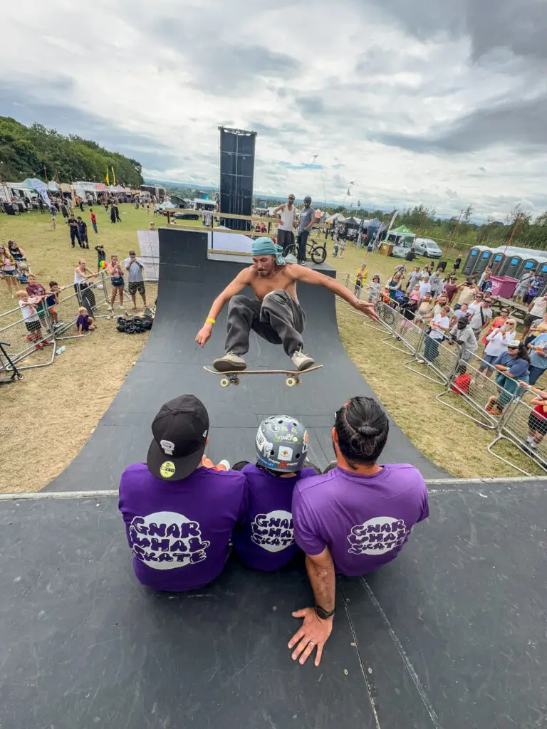 Skateboarder performs jump over three people sitting on a halfpipe during a skateboarding session.