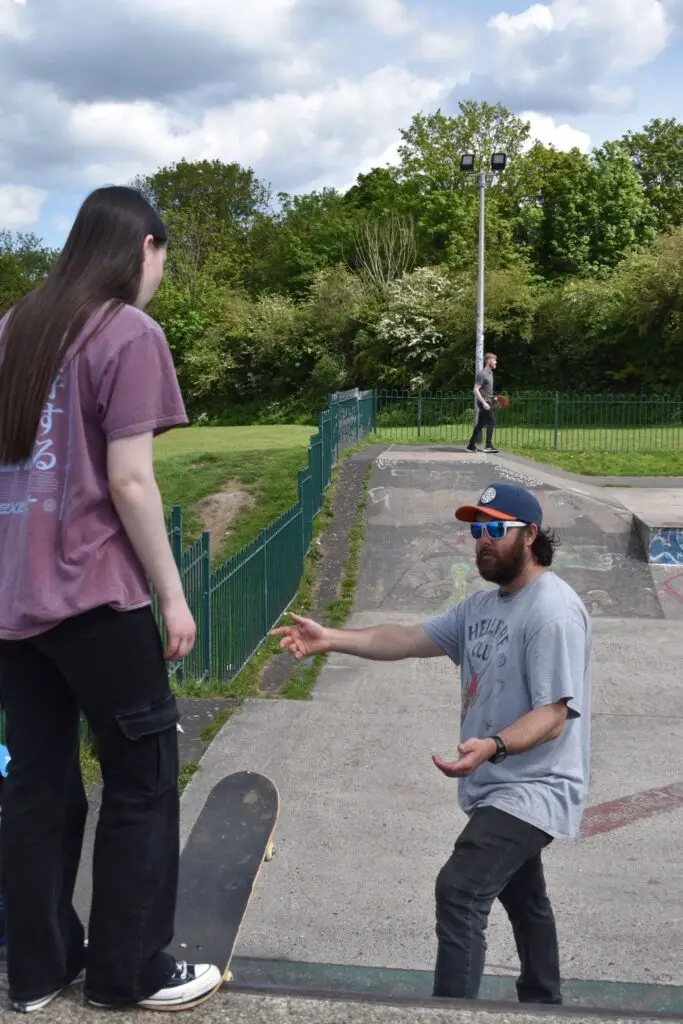 Skateboard coach assisting a woman as she prepares to drop in on a ramp during a lesson.