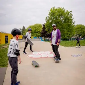 Skateboard coach teaching two students at Cozenton Skatepark during a skateboarding lesson.