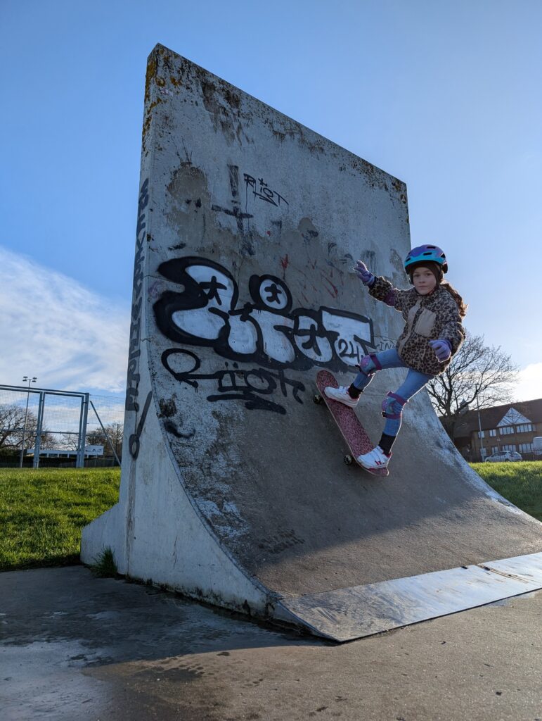 Young girl riding up a vert wall on a skateboard during a skateboarding lesson.